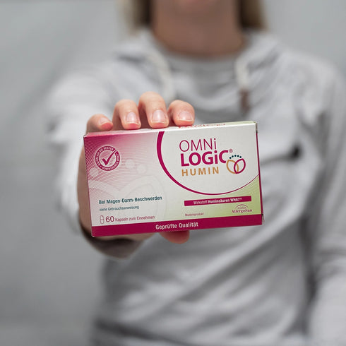 Eine Person hält eine Packung OMNi-LOGiC HUMIN in die Kamera
